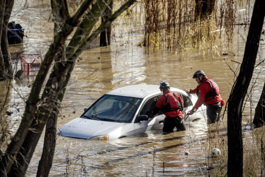 Search and rescue workers investigate a car surrounded by floodwater as heavy rains caused the Guad...