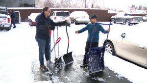 two men stand in the snow with four shovels