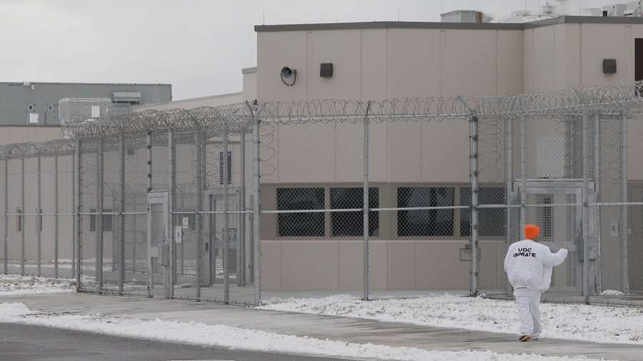 fences and buildings with an inmate walking on a snowy sidewalk...