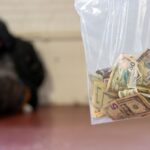 A person arrested waits for processing as a law enforcement officer holds a bag of cash, which was seized during an investigation into drug trafficking. (Salt Lake City Police Department)