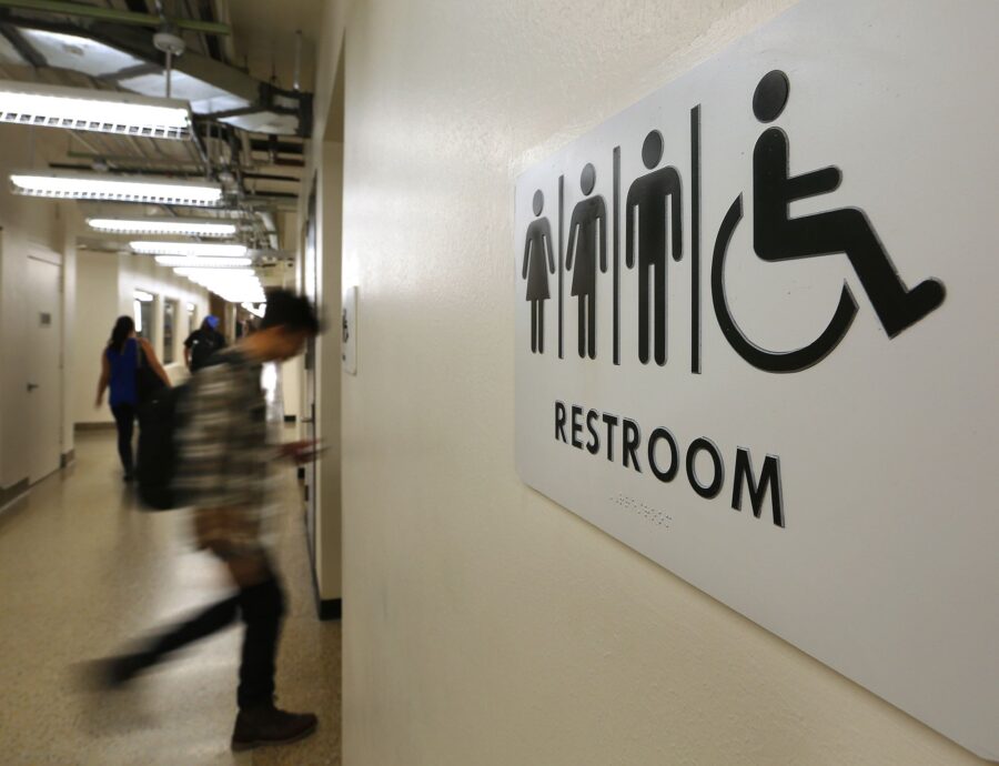 Students pass by a sign for a unisex bathroom next to the men's and women's restroomS at the Univer...