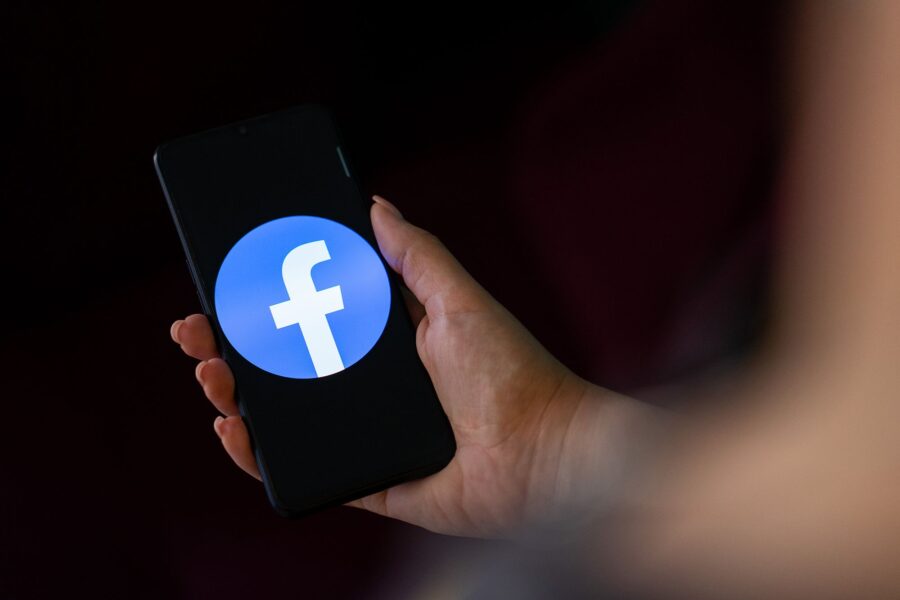 A person holds a phone with the Facebook logo on it...
