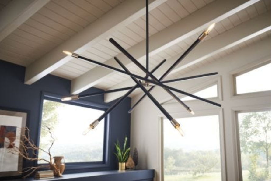 Modern chandelier hanging from a white slanted ceiling with windows in the backgruond...
