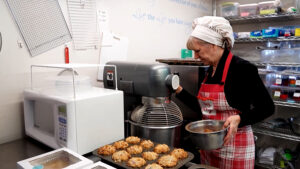 a woman in a cooking apron looks at a mixer and baked goods