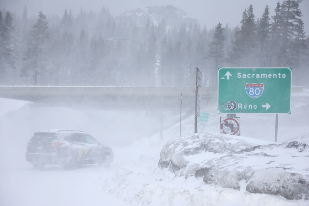 A vehicle drives through blowing snow near Interstate 80 (I-80) in the Sierra Nevada mountains at t...