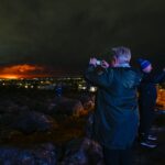 People on the outskirts of Reykjavik take pictures of the orange colored sky as molten lava flows out from a fissure on the Reykjanes peninsula north of the evacuated town of Grindavik, western Iceland, on March 16. (Halldor Kolbeins, AFP/Getty Images)
