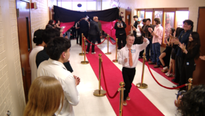 Young prom goers dressed up walking down a red carpet