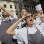 Restaurant workers in the Flatiron district of Manhattan take a break to view the solar eclipse, Monday, April 8, 2024, in New York. (AP Photo/John Minchillo)
