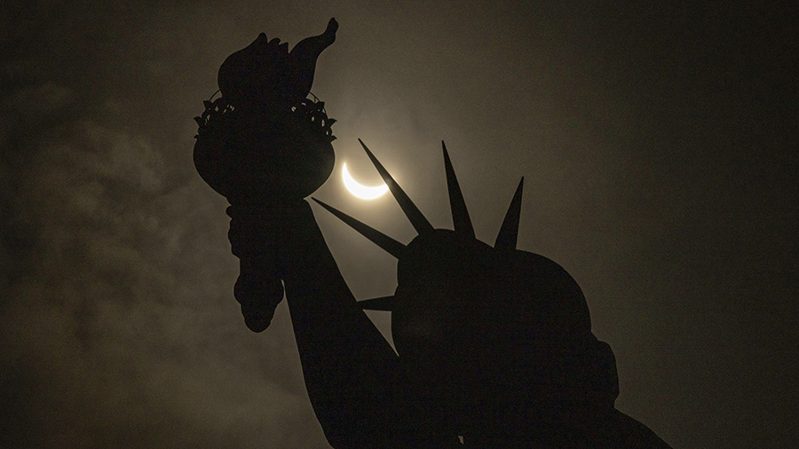 The moon partially covers the sun behind the Statue of Liberty during the a solar eclipse on the Li...