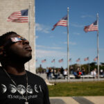 WASHINGTON, DC - APRIL 08: Zion Edwards of Grand Prairie, Texas, looks at the solar eclipse through two pair of mylar filter glasses near the base of the Washington Monument on the National Mall on April 08, 2024 in Washington, DC. People have traveled to areas across North America that are in the "path of totality" in order to experience the eclipse today, with the next total solar eclipse that can be seen from a large part of North America won't happen until 2044.  (Photo by Chip Somodevilla/Getty Images)