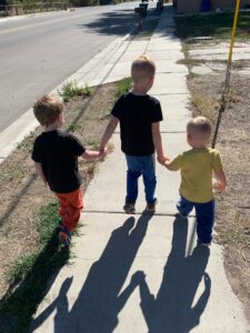 The three boys walking down a sidewalk together, holding hands.