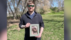 Travis Mundt holding a photo of his dog Oliver, who was killed after rushing into high water in 2023. 