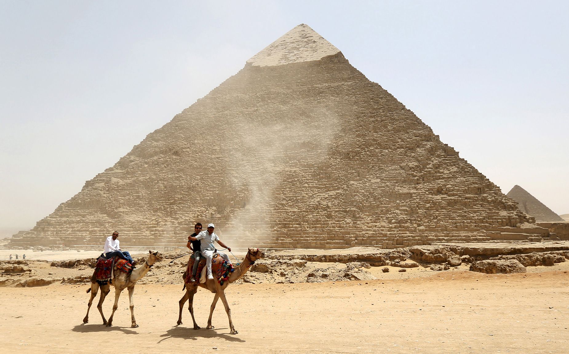 Tourists ride on camels next to the Pyramid of Khufu on the Great Pyramids of Giza, on the outskirt...