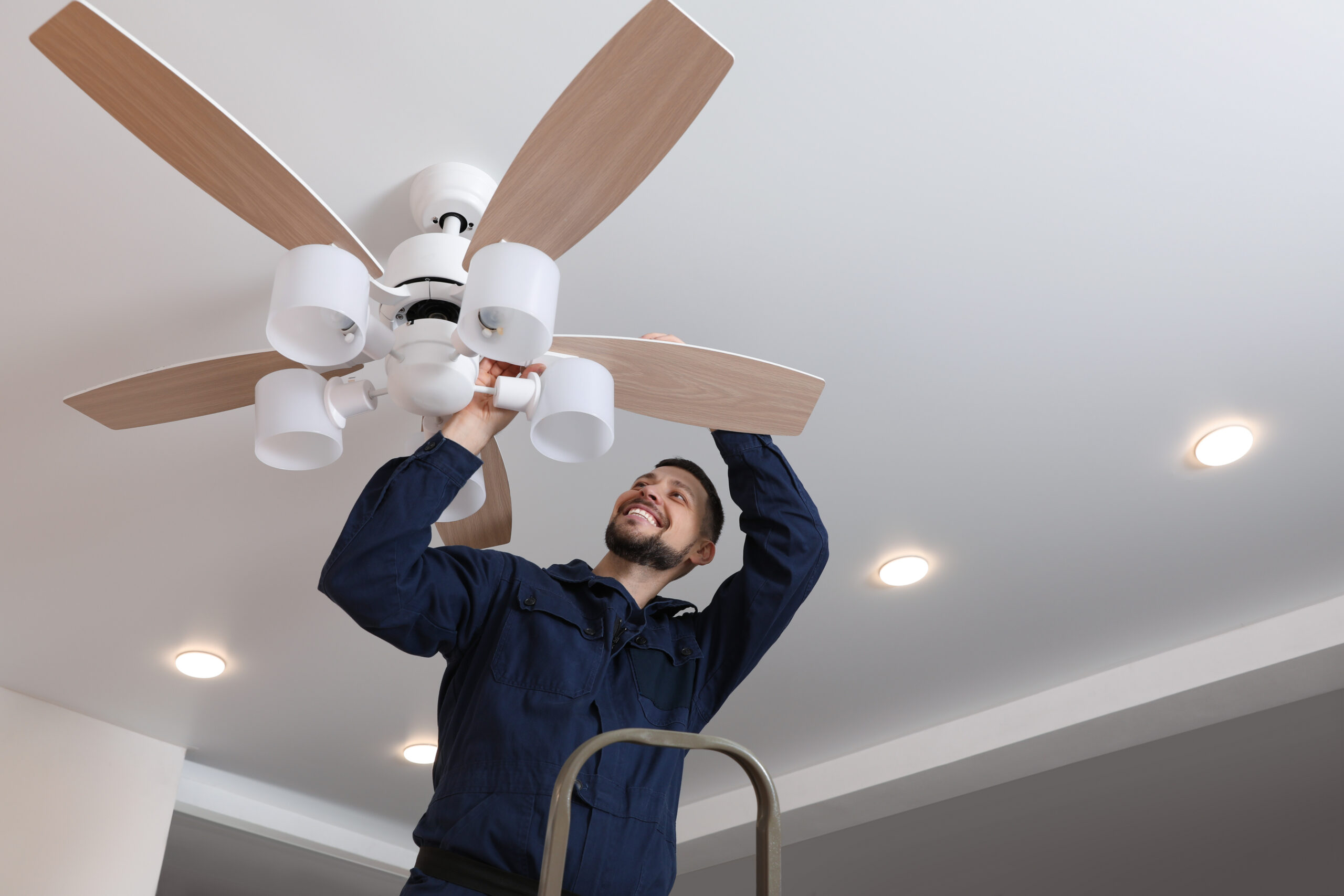 Electrician repairing ceiling fan with lamps indoors...