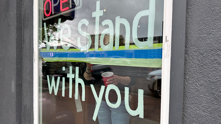 An employee at The Fellas Barber Shop painting "We stand with you" on the store's window to show su...