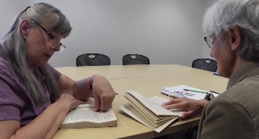 two women sit at a table reading...